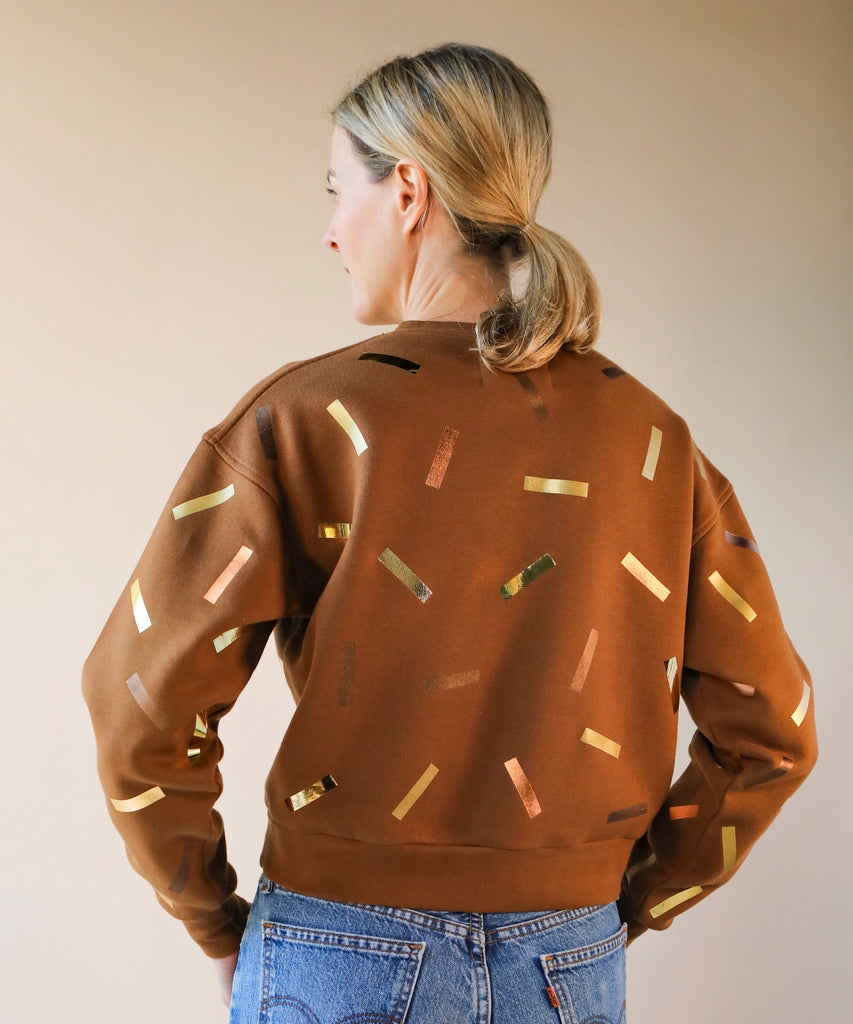 a woman wears a brown sweatshirt with gold and bronze confetti sprinkle print design