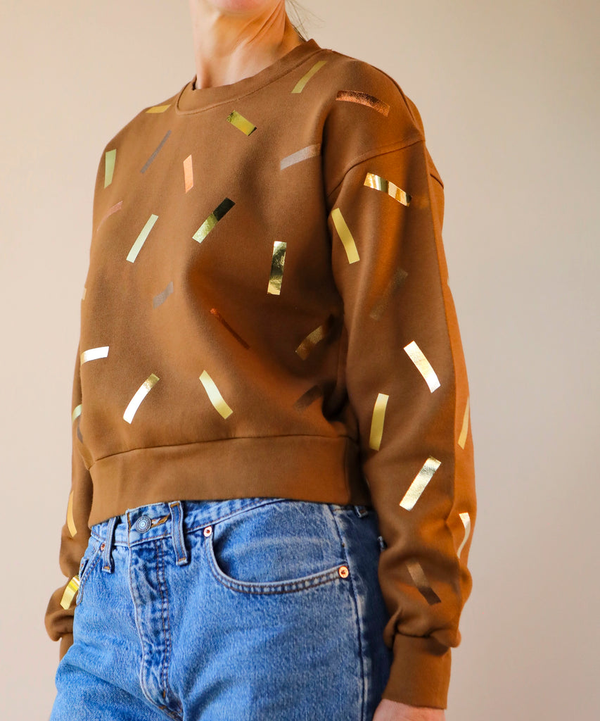 a woman wears a brown sweatshirt with gold and bronze confetti sprinkle print design
