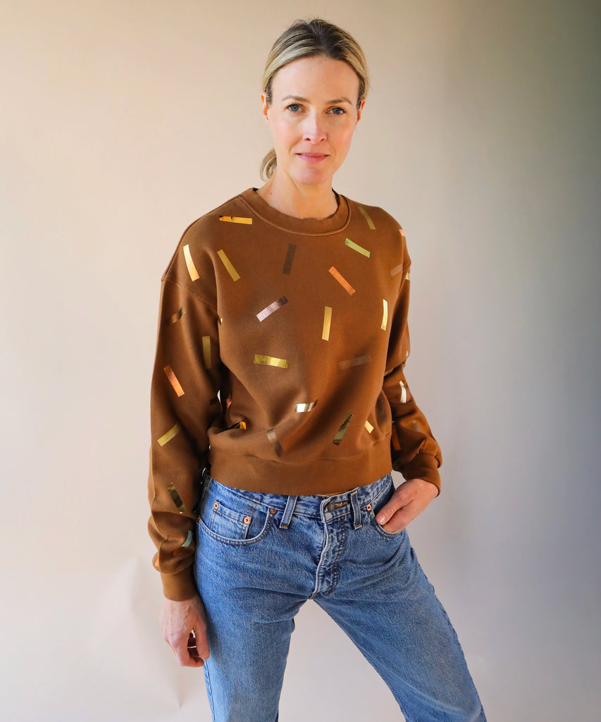 a woman wears a brown sweatshirt with gold and bronze confetti sprinkle print design
