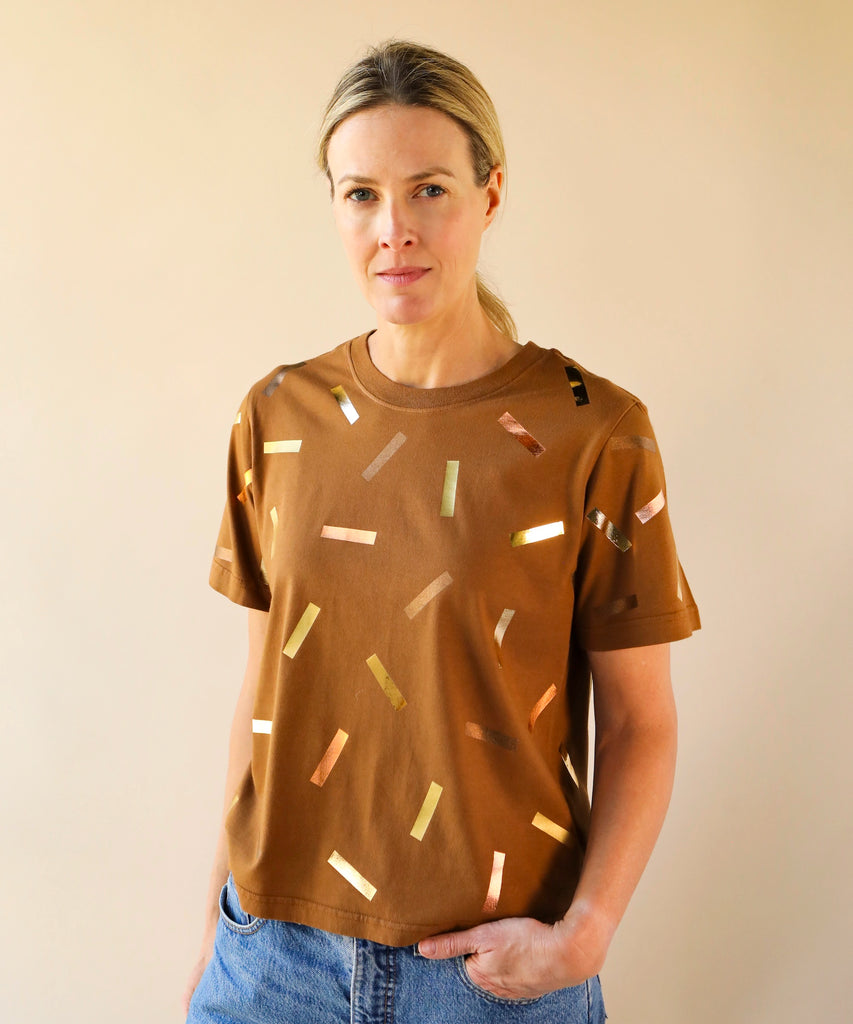 a woman wears a boxy cotton tshirt in tobacco brown with gold confetti sprinkle graphic print
