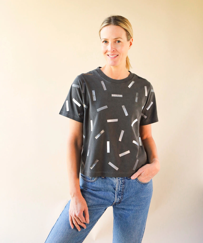 a woman wearing a boxy cotton tshirt in dark grey with silver confetti sprinkle graphic print
