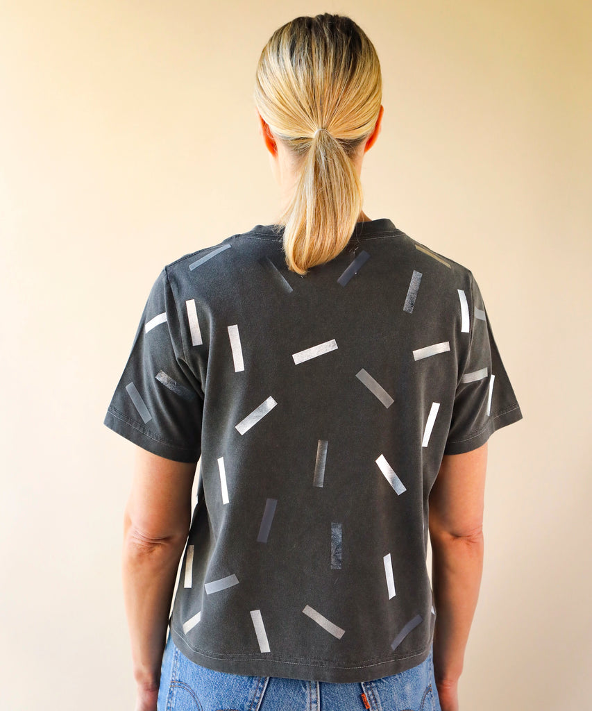 a woman wearing a boxy cotton tshirt in dark grey with silver confetti sprinkle graphic print