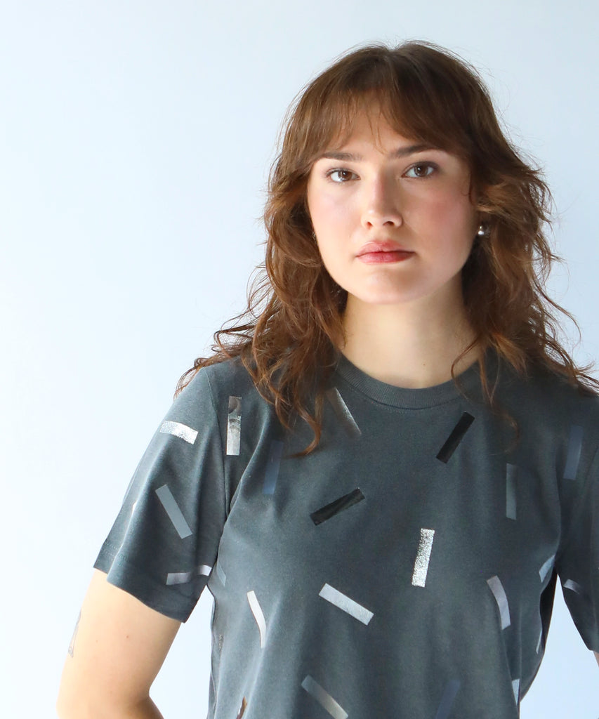 a woman wearing a boxy cotton tshirt in dark grey with silver confetti sprinkle graphic print