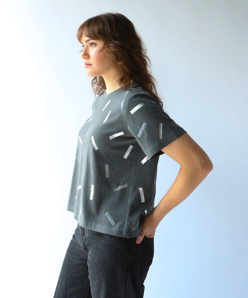 a woman wearing a boxy cotton tshirt in dark grey with silver confetti sprinkle graphic print
