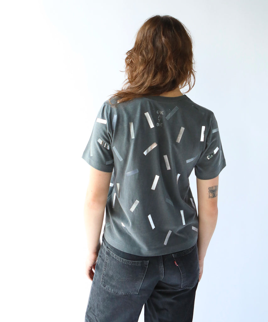 a woman wearing a boxy cotton tshirt in dark grey with silver confetti sprinkle graphic print