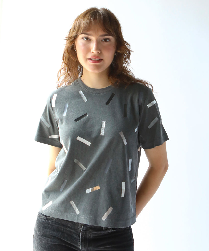 a woman wearing a boxy cotton tshirt in dark grey with silver confetti sprinkle graphic print