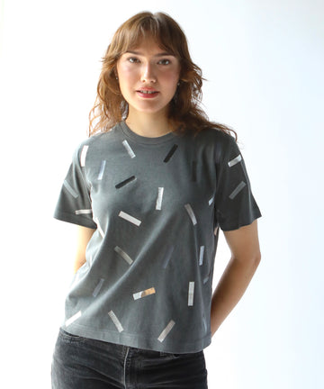 a woman wearing a boxy cotton tshirt in dark grey with silver confetti sprinkle graphic print