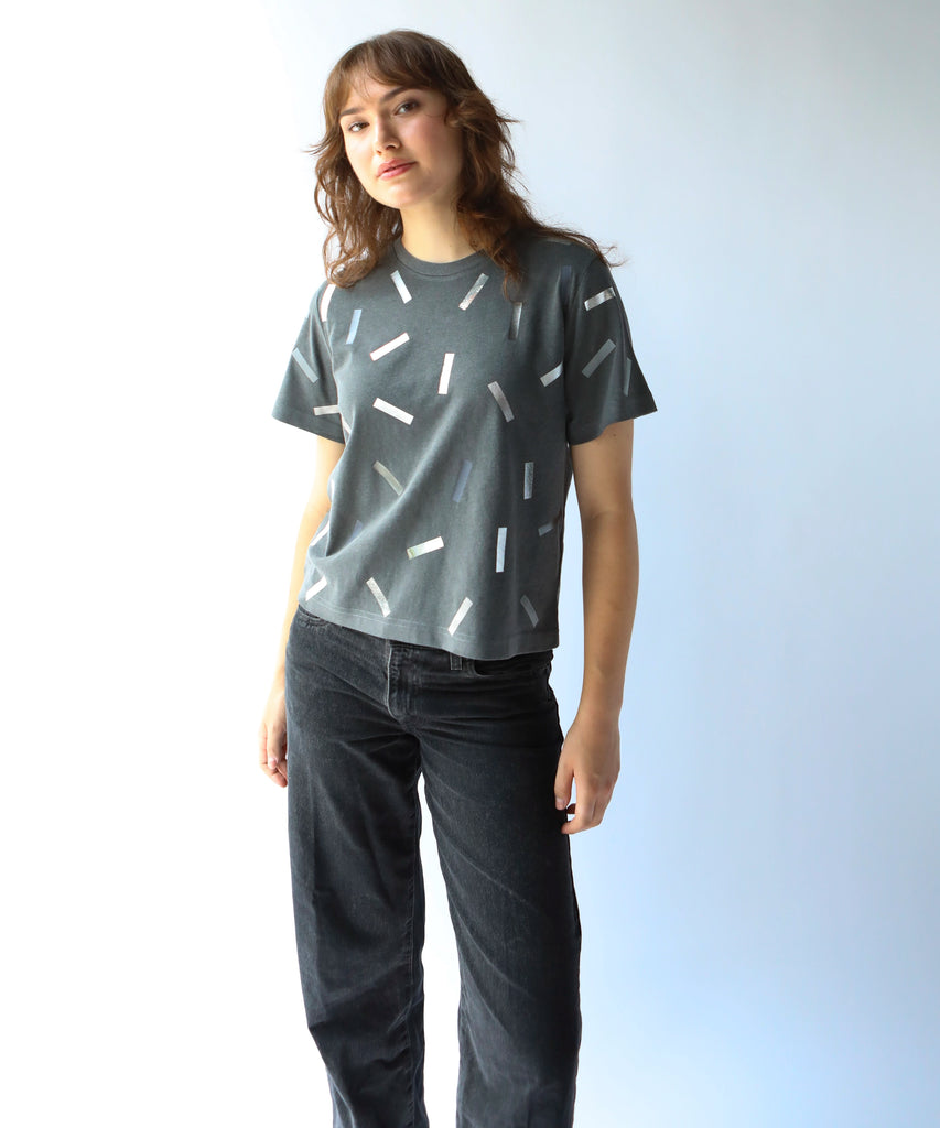 a woman wearing a boxy cotton tshirt in dark grey with silver confetti sprinkle graphic print