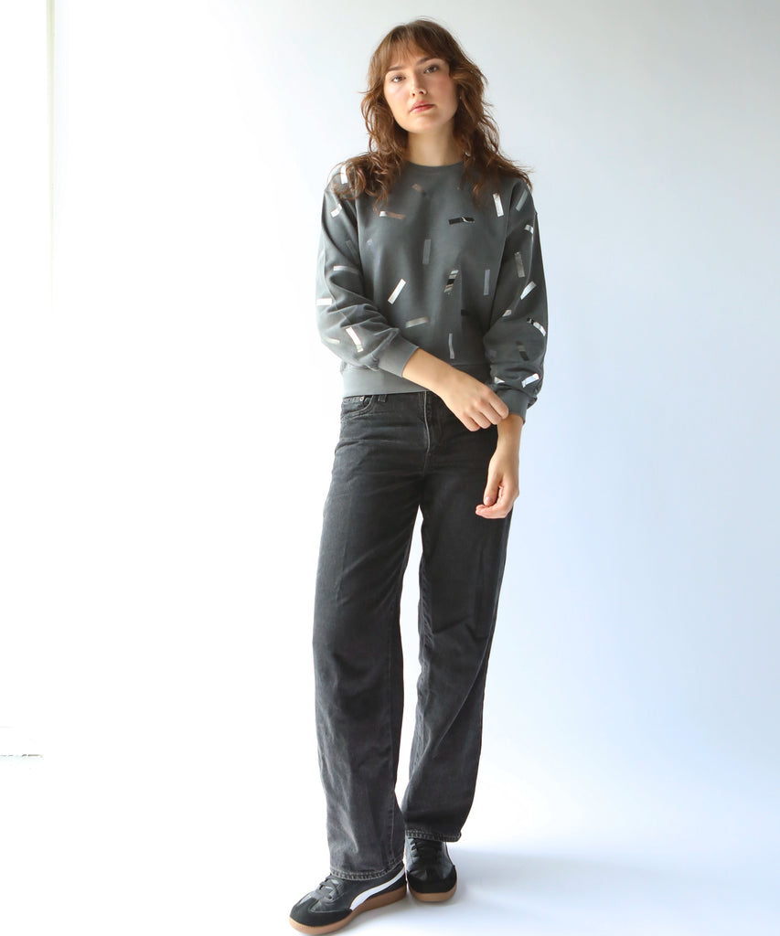 a woman wears a cotton sweatshirt in grey with silver confetti sprinkle graphic print with grey jeans
