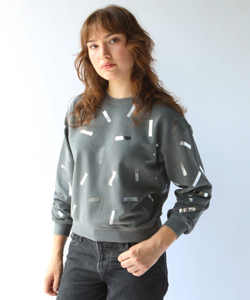 a woman wears a cotton sweatshirt in grey with silver confetti sprinkle graphic print