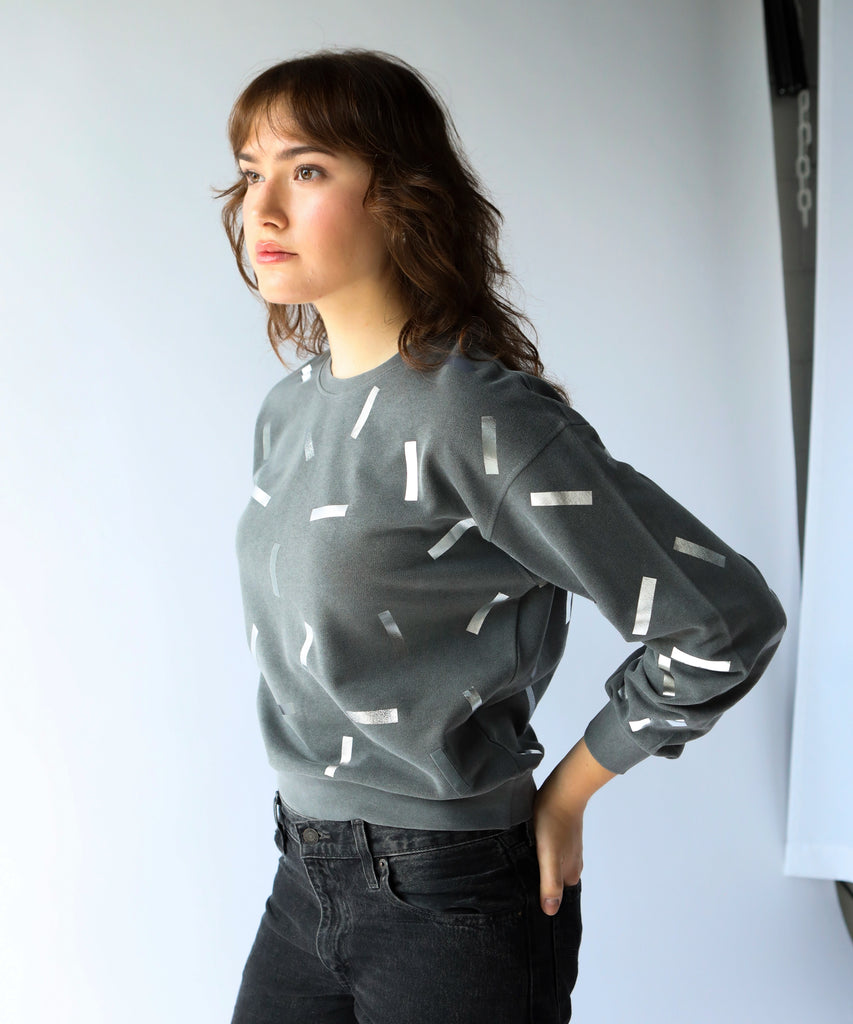 a woman wears a cotton sweatshirt in grey with silver confetti sprinkle graphic print