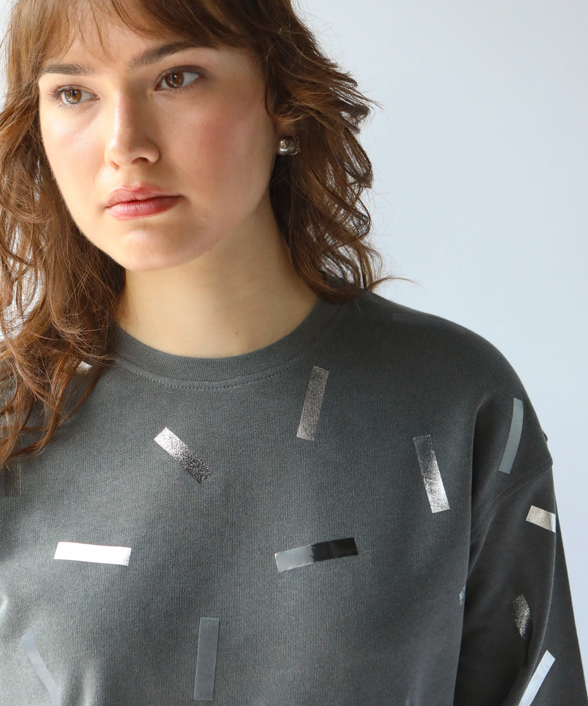 a woman wears a cotton sweatshirt in grey with silver confetti sprinkle graphic print
