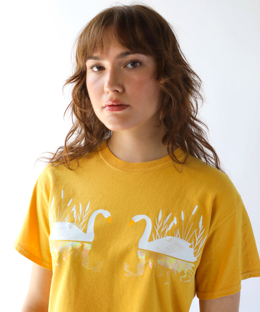 woman wearing a cotton tshirt in mustard yellow with two white swans graphic